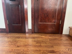 Hardwood floors and vintage wooden doors with trim missing near staircase