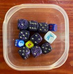 Multiple types of dice from board games in small IKEA Pruta food container
