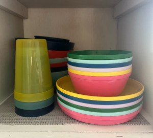 Target Pillowfort kid dishes in bright colors, cups, bowls, and plates stacked inside cabinet