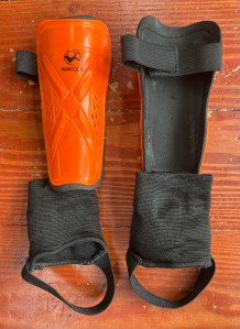 Outfun Youth Soccer Shin Guards in black and orange front and back with hook and loop closure shown