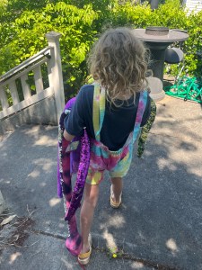 Eleven year old girl wearing rainbow overall shorts carrying five stuffed snakes