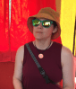 Woman wearing turqousie Goodr sunglasses and orange sun hat against red backddrop