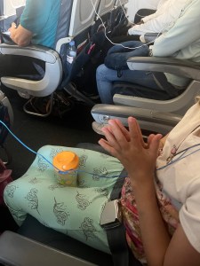 Eleven year old girl in airplane seat with Nuk hard spout sippy cup in lap