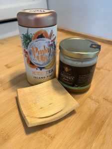 Pinky Up tea tin with Marie's Bees Mother's Honey jar and wooden spoon rest on light wooden stove top burner cover