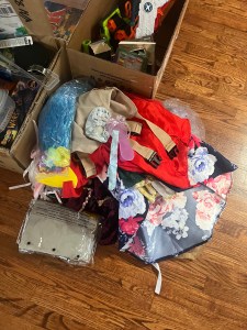 Pile of donated children's clothing and items next to cardboard box of