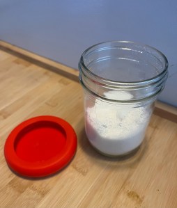 Food Huggers red reusable silicone jar lid next to jar of sugar