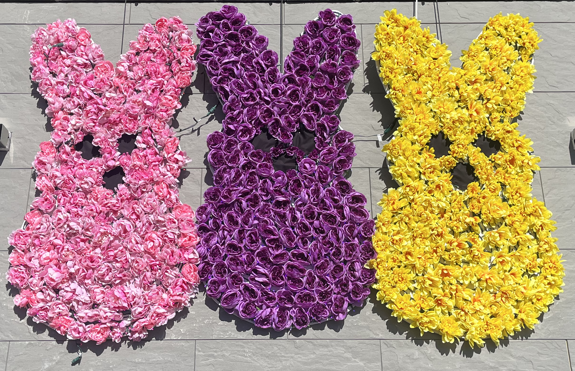 Peeps made from pink, purple, and yellow flowers on side of gray building