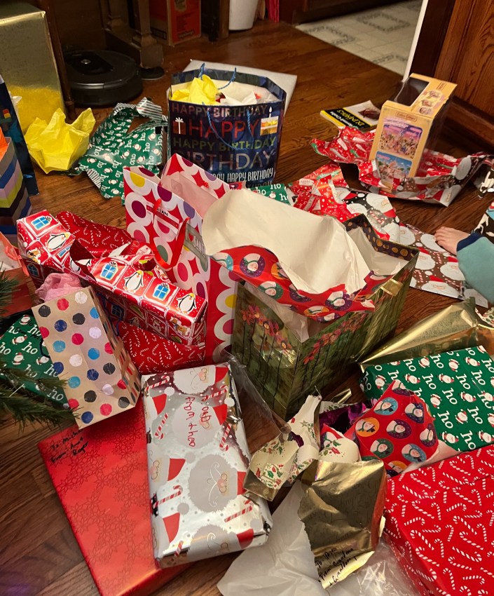 Pile of opened and wrapped holiday gifts on hardwood floor at Christmas