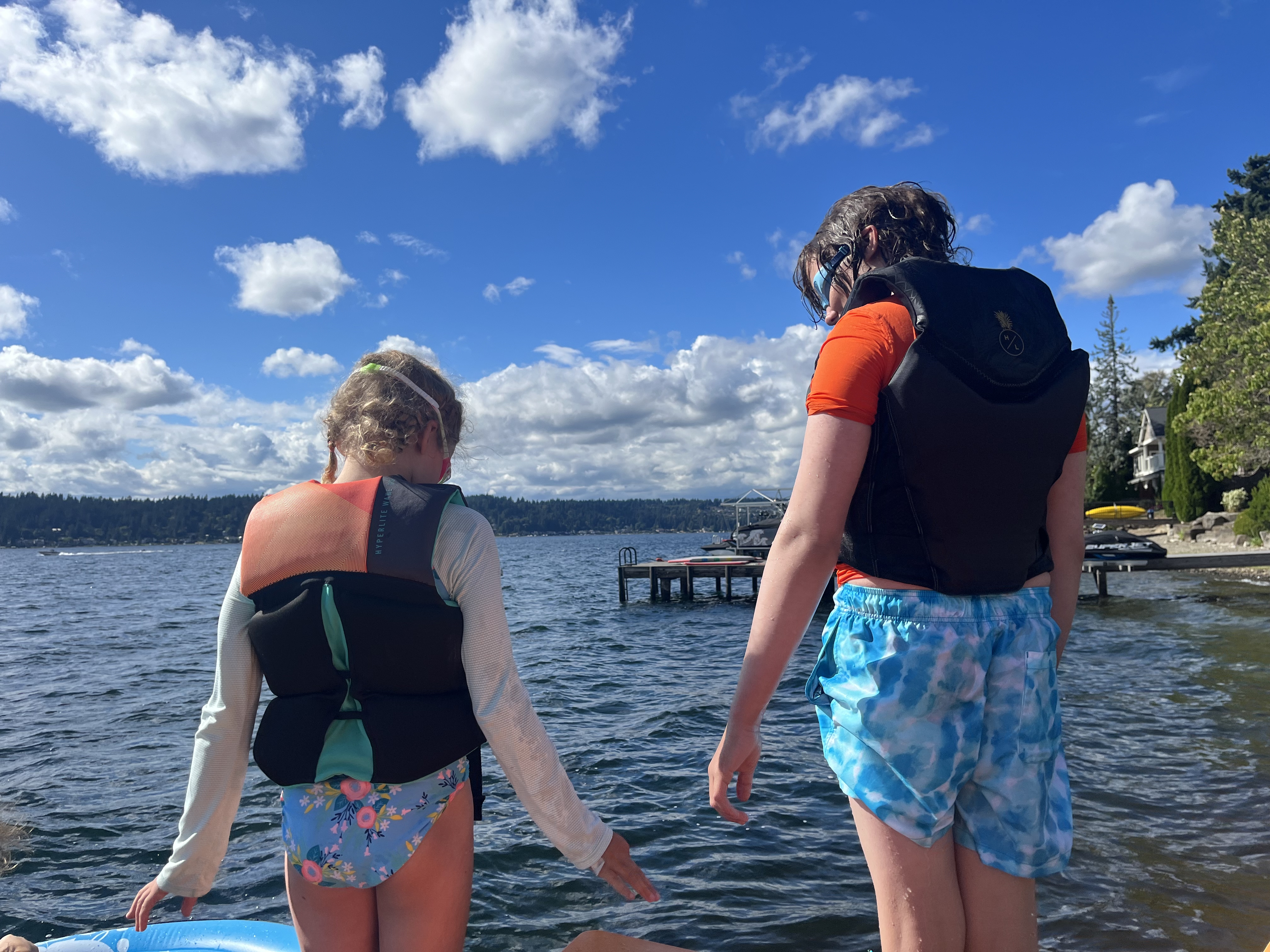 Girl and boy wearing life jackets getting ready to jump into lake on sunny summer day
