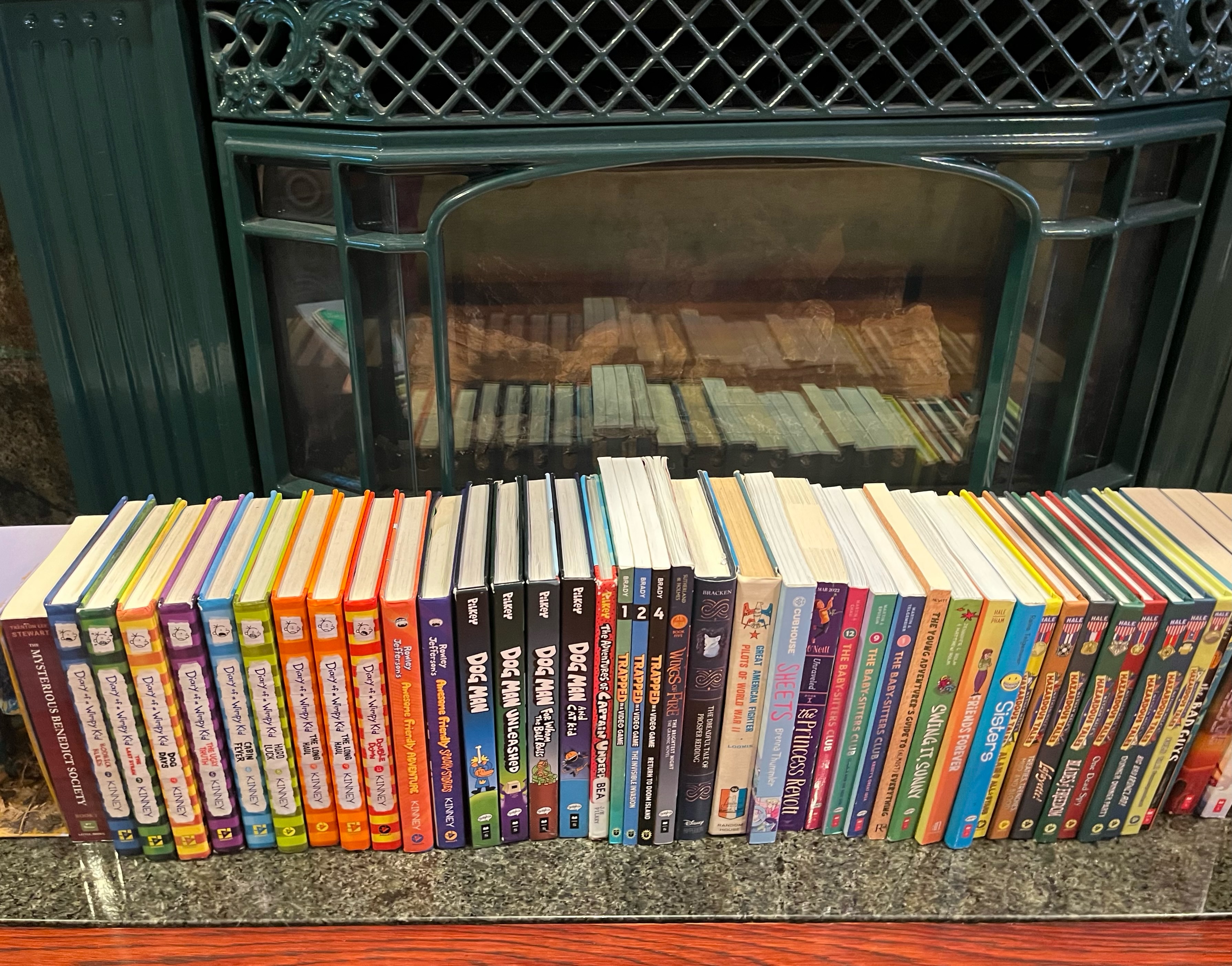 Books stored on fireplace mantel in a row