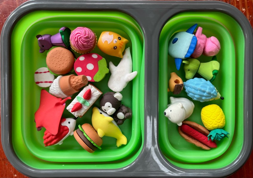 Green collapsible lunch box filled with brightly colored animal erasers in polar bear, pink poodle, yellow dolphin, brown monkey and other shapes